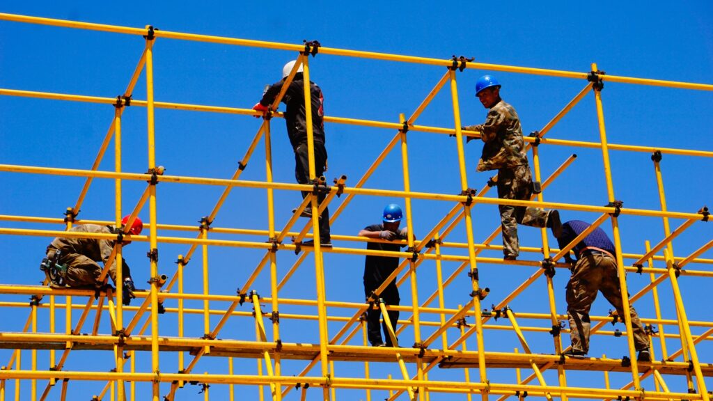 3 men standing on yellow metal fence during daytime